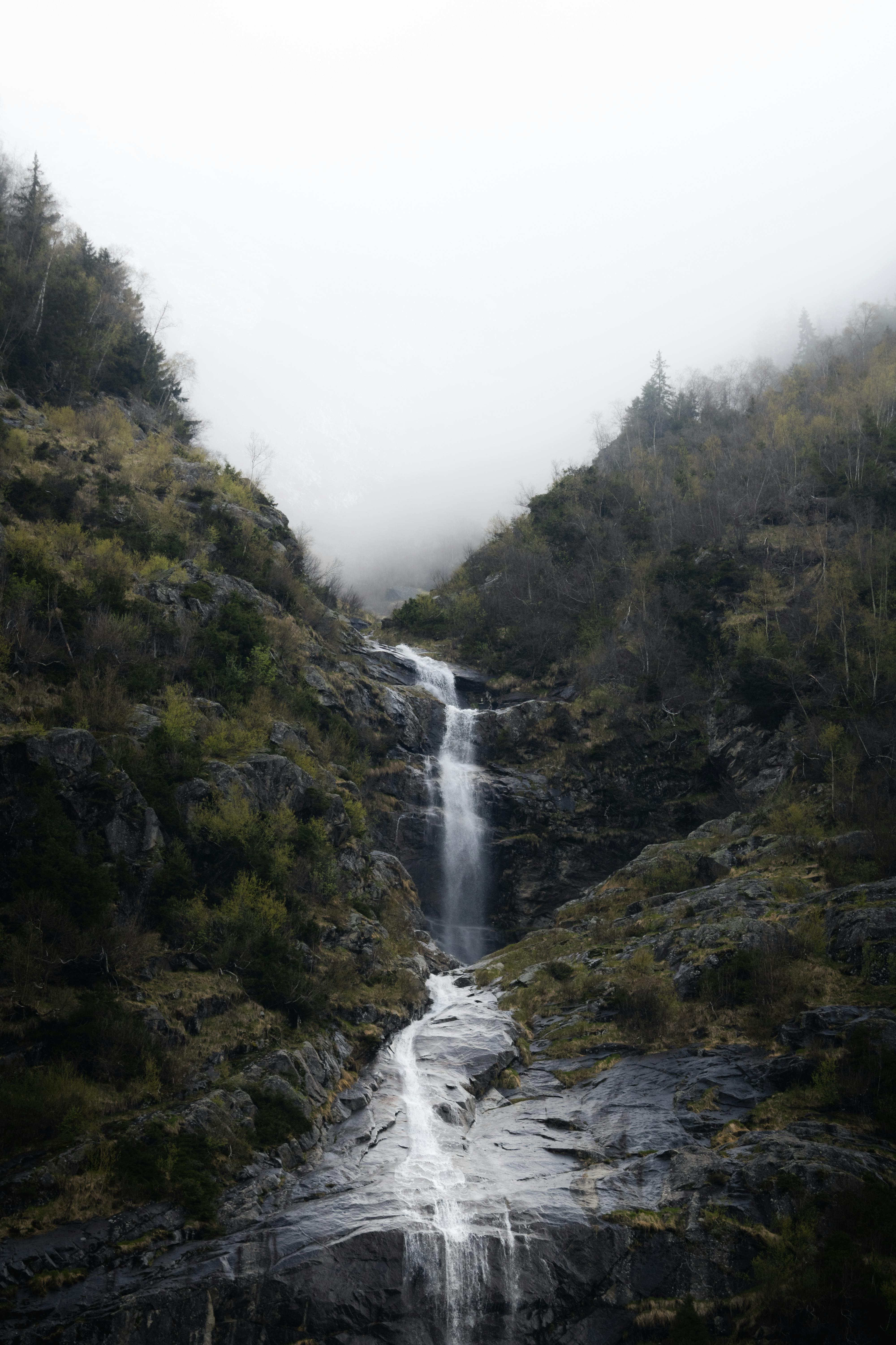 a waterfall is seen in the foggy mountains