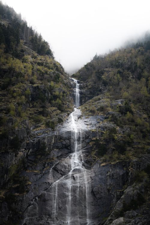 Free Capture the serene beauty of a misty waterfall in Ginzling, Tirol, set against lush green mountains and soothing clouds. Stock Photo