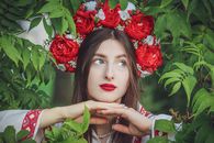 Close-up portrait of a woman with a floral headdress and traditional Ukrainian attire in nature.