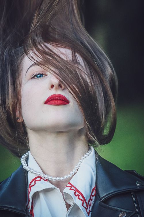 Free Close-up portrait showcasing elegant woman with red lips and pearl necklace outdoors. Stock Photo