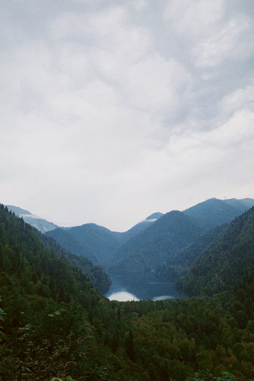 Free Scenic view of a serene lake surrounded by lush mountains under a cloudy sky. Stock Photo