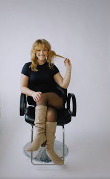 Portrait of a smiling woman with curly hair sitting confidently in a studio chair.