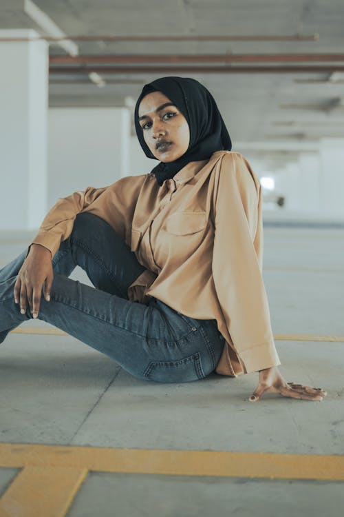 Young Woman in Hijab Beige Blouse and Jeans Sitting on the Floor of a Parking Garage