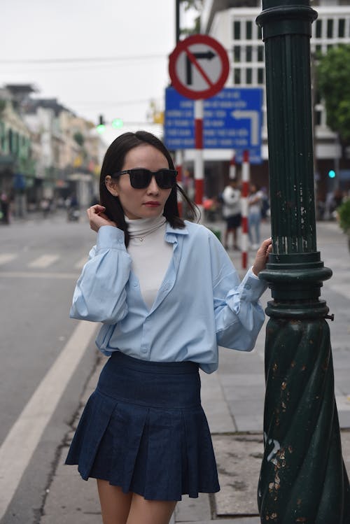 Model in a Blue Blouse Over a White Turtleneck and a Pleated Mini Skirt Standing on the Sidewalk