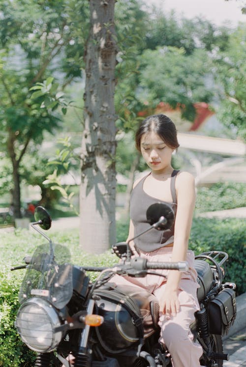 Young Woman in Black Top Posing on Motorcycle in Park