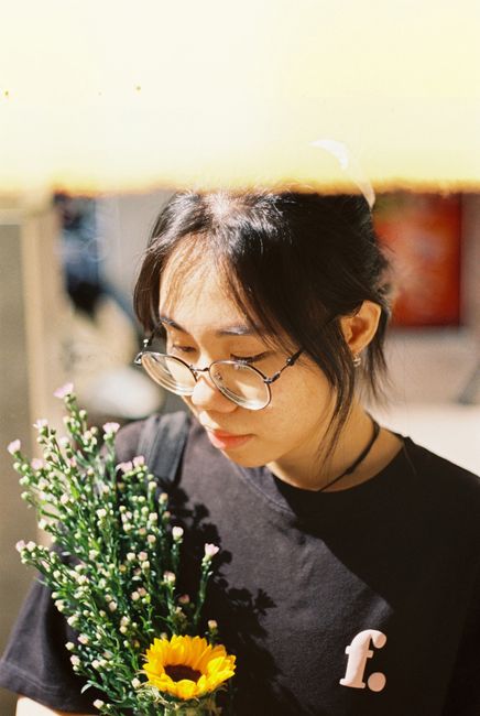 Asian woman holding flowers in Ho Chi Minh City, wearing eyeglasses and black t-shirt.