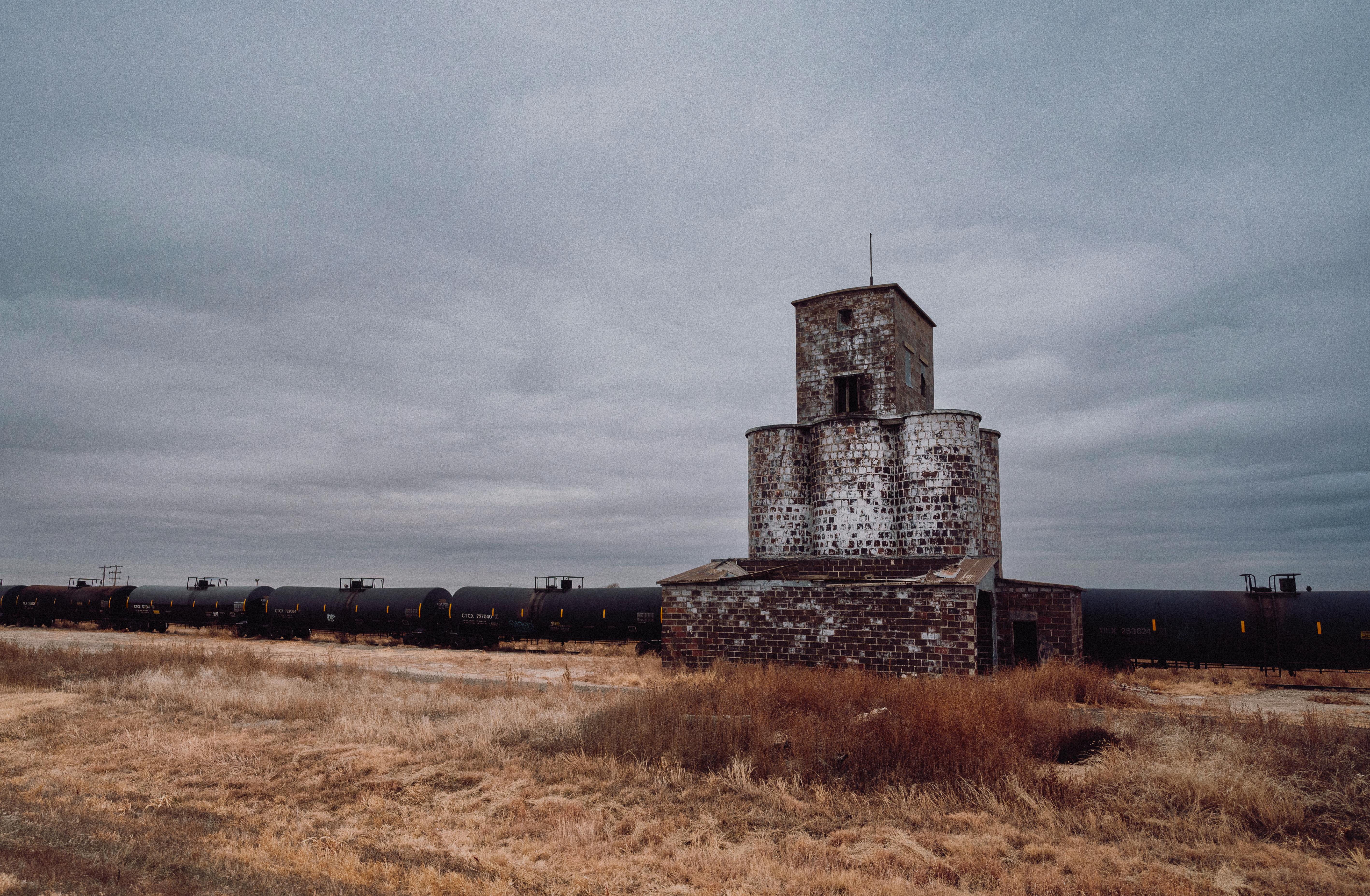 Deserted grain elevator with train tank cars in rural Kansas landscape.