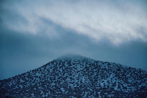 Free A serene view of a snowcapped mountain under a dramatic, cloudy sky at dawn. Stock Photo