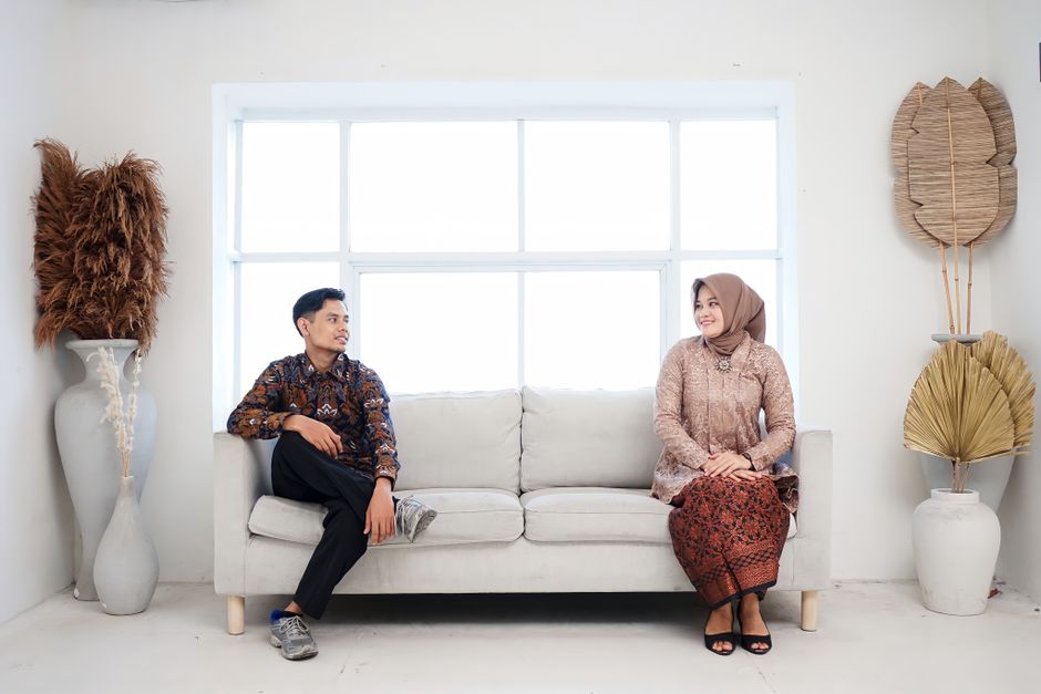 A couple in traditional attire sits on a sofa in a minimalist living room.