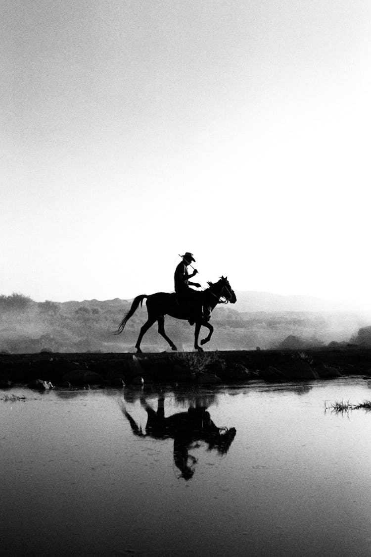 Cowboy Riding Horse Near Water In Black And White