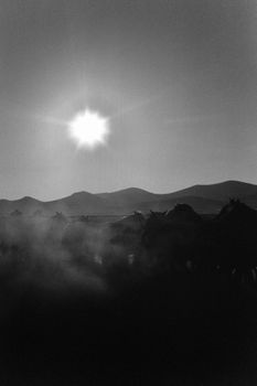 Captivating black and white landscape of mountains and sun with atmospheric fog.