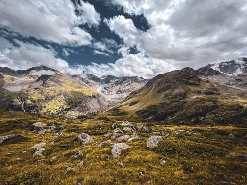 Free A breathtaking view of alpine mountains under a vibrant cloudy sky, featuring lush greenery. Stock Photo