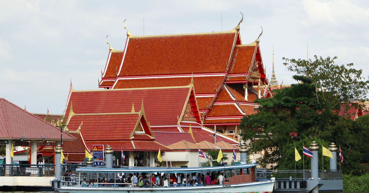 A passenger boat on the Chao Phraya river passing a temple in Bangkok.