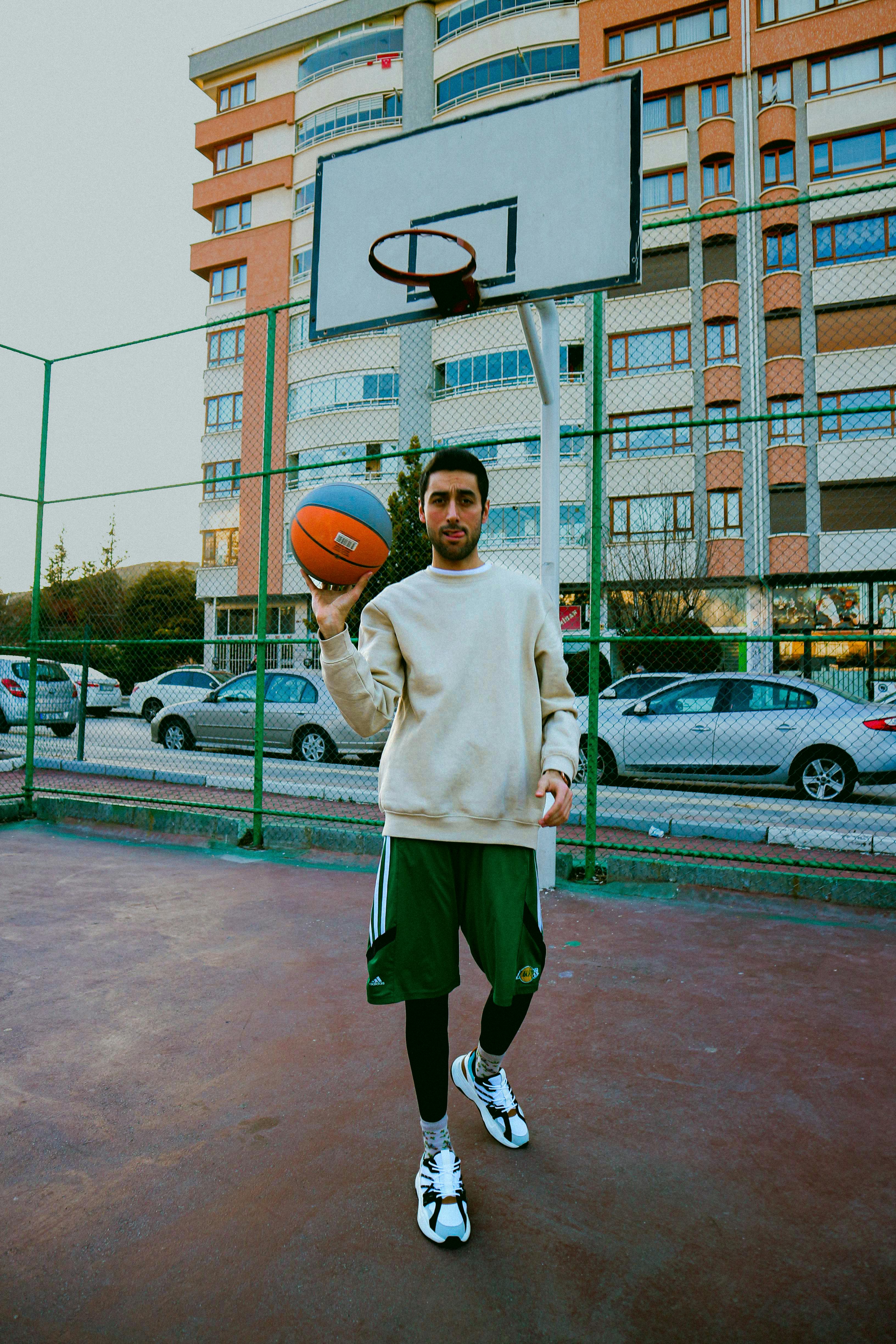 Man holding a basketball in a city court, set against residential buildings.