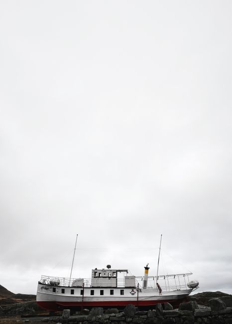 A vintage ship stranded on rocky terrain under a vast gray sky, creating a dramatic maritime scene.