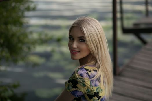 Relaxed portrait of a blonde woman smiling by a lake in Prague, capturing the essence of summer serenity.