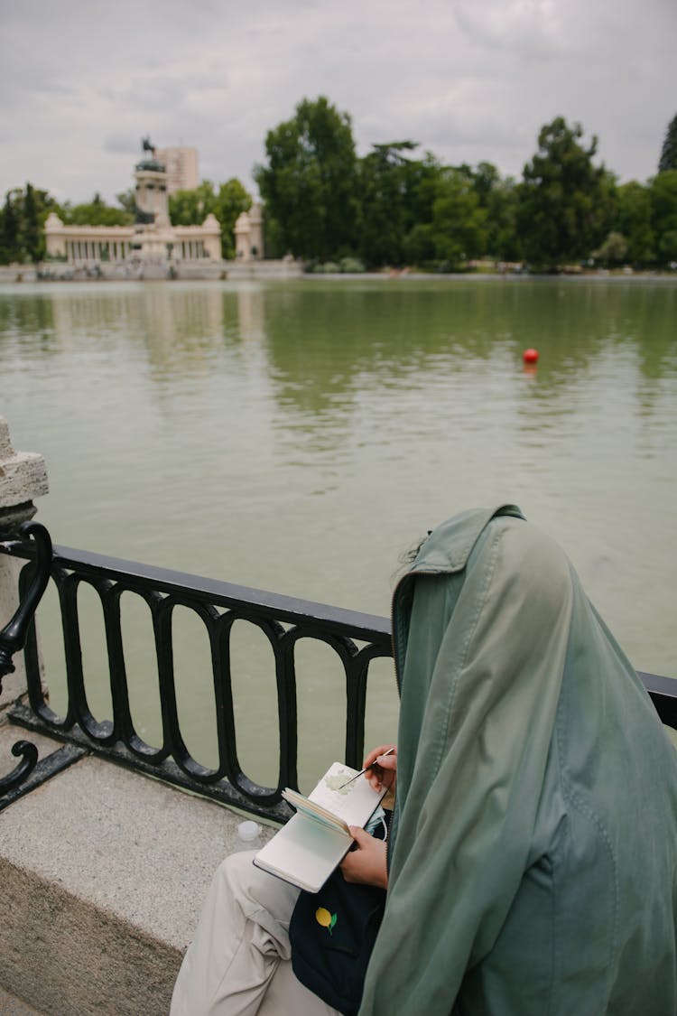 Person With Jacket On Head Sitting And Drawing