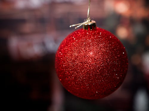 A big shinny red Christmas ball hanging on a golden string against a blurred moody background. Holiday season background with empty space for text