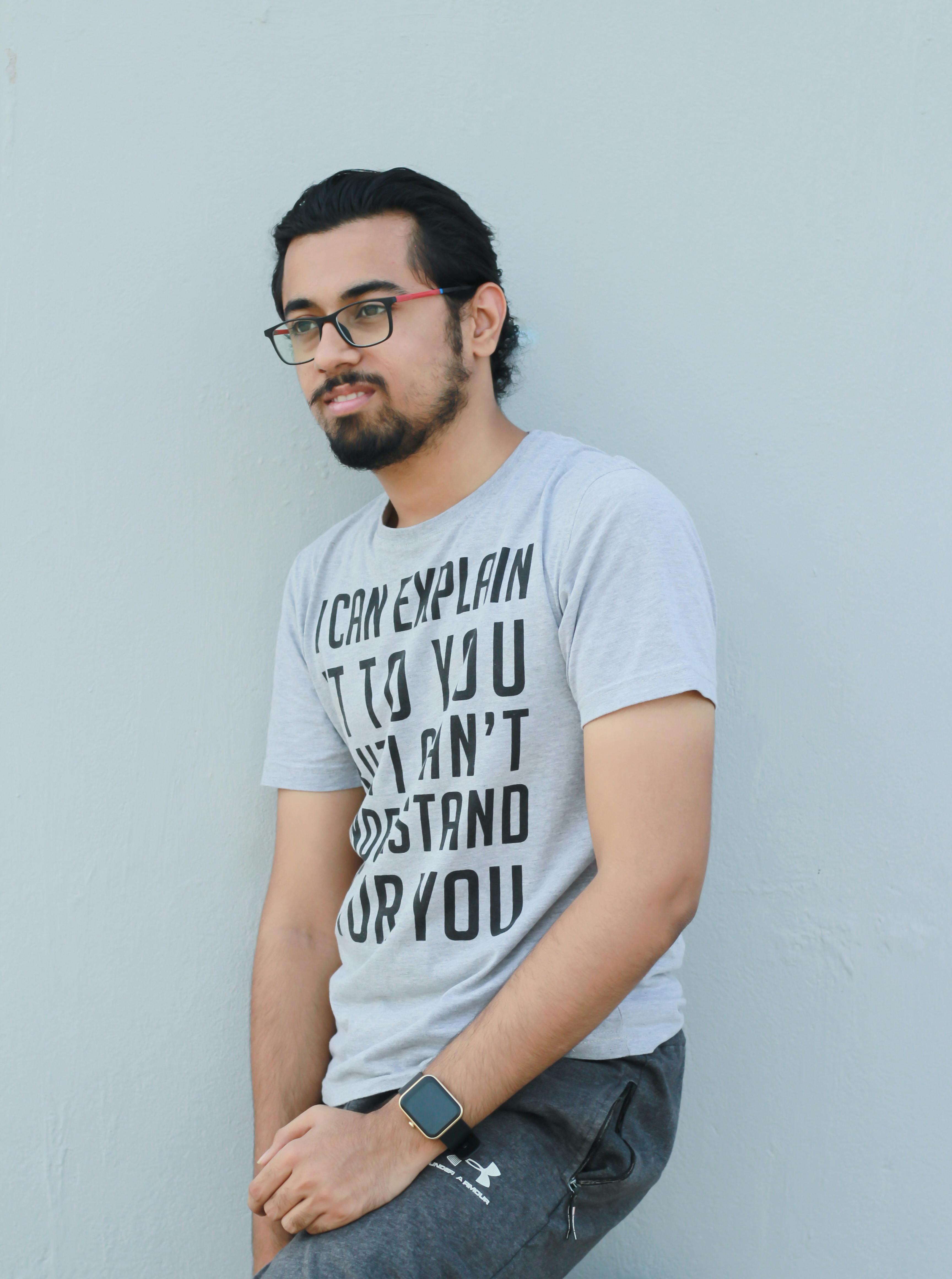 Stylish man with eyeglasses leaning against a wall, wearing a graphic t-shirt and smartwatch.