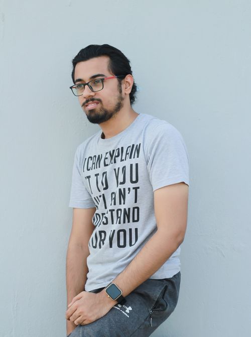 Free Stylish man with eyeglasses leaning against a wall, wearing a graphic t-shirt and smartwatch. Stock Photo