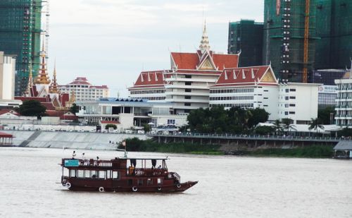 Free Scenic view of a traditional wooden boat sailing past the Phnom Penh skyline along the riverfront. Stock Photo