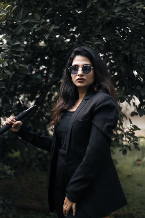 Young Elegant Woman in a Black Outfit and Sunglasses Standing Outside 