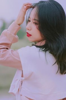 Side profile of a young Asian woman with black hair in an outdoor setting, exuding simplicity and elegance.