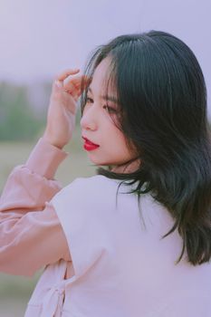 Serene portrait of an Asian woman with black hair captured in natural light, wearing casual attire outdoors.