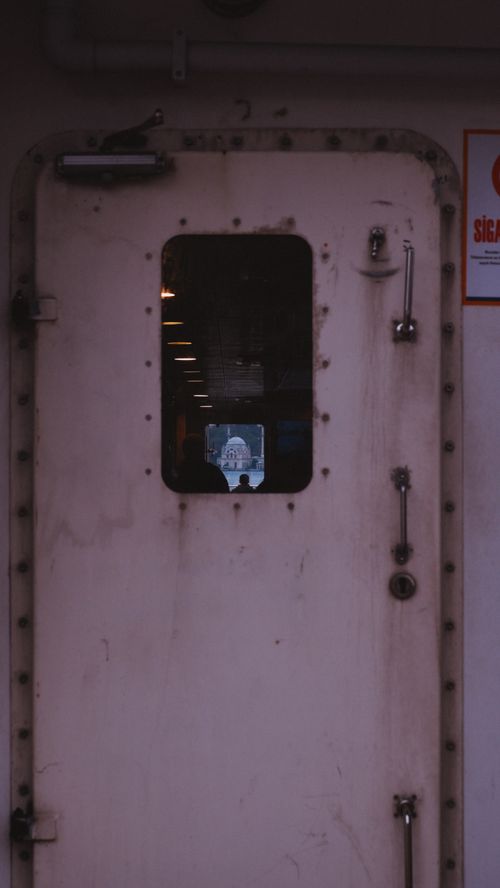 Free Close-up of a metal door with a window showing an interior and distant view. Stock Photo