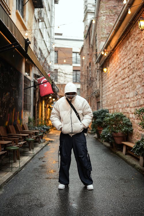 Model in a Padded White Jacket and Loose Black Cargo Pants Standing in an Alley