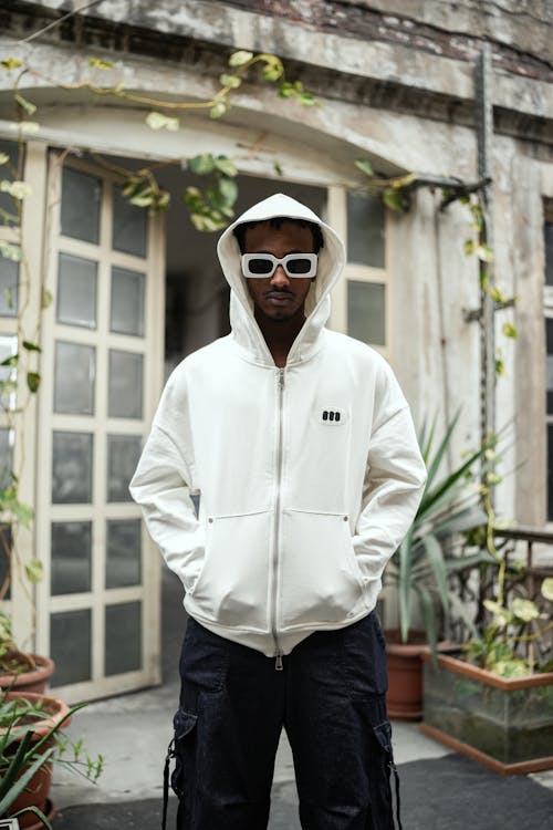 Model in Thick Frame Sunglasses Wearing a White Zip Up Hoodie and Black Cargo Pants Posing on a Balcony Free Stock Photo
