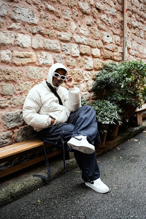 Model in Thick Frame Sunglasses Wearing a Padded White Jacket and Wide Cargo Pants Sitting on Bench