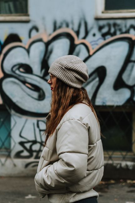 Profile of a young woman in warm clothing standing by a graffiti-covered wall in Bucharest.