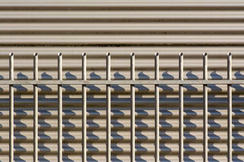 Free Close-up of a metal fence with shadows on a corrugated surface, showcasing industrial design. Stock Photo