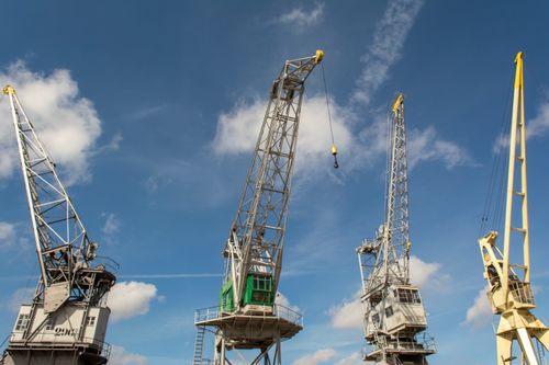 Free Multiple harbor cranes standing tall under a bright blue sky with fluffy clouds. Stock Photo