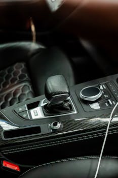 Close-up of a luxury car interior highlighting a carbon fiber gear shift and leather seats.