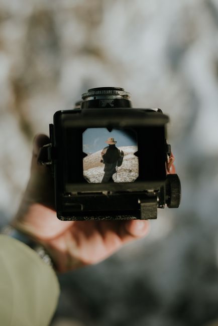 View through a vintage camera depicting an outdoor scene with a person wearing a hat.