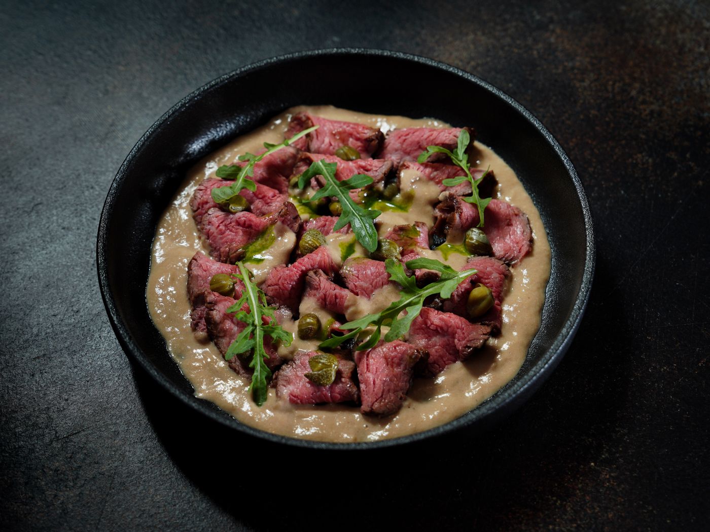 Carne cruda con rucola su una crema, in una ciotola scura