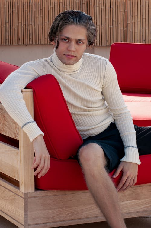 Man Wearing a White Turtleneck, Sitting on Red Wooden Furniture
