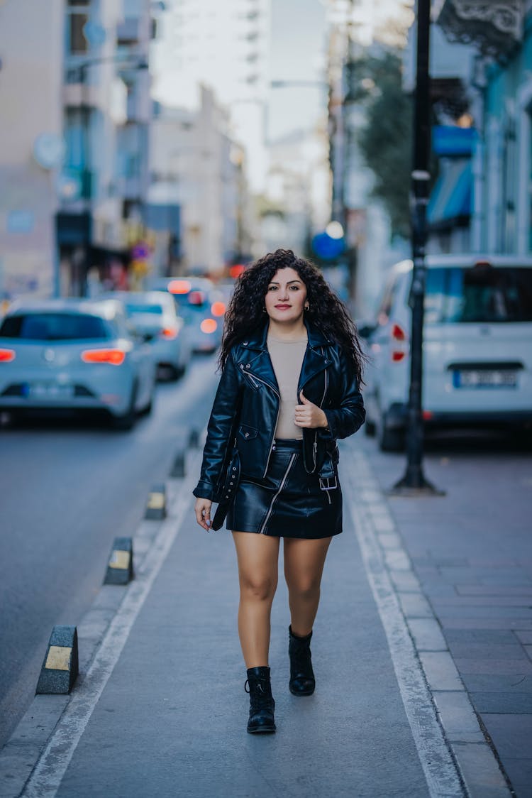 Young Woman In A Skirt And Leather Jacket Walking On The Street 