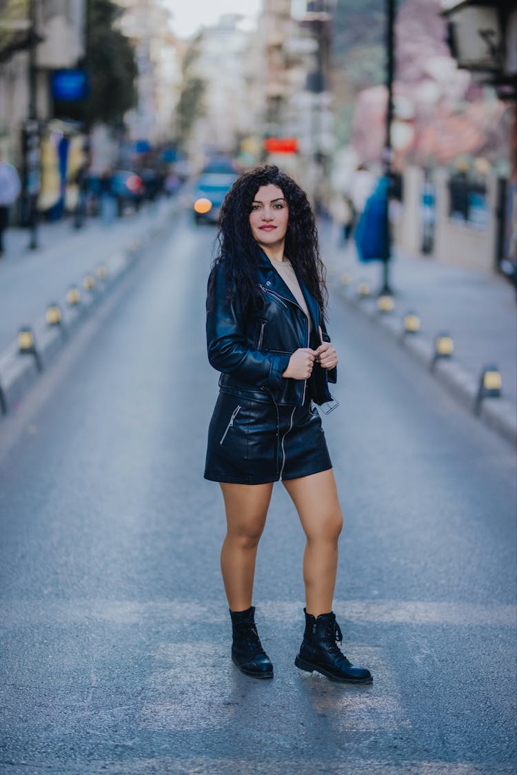 Young Woman In A Skirt And Leather Jacket Standing On The Street 