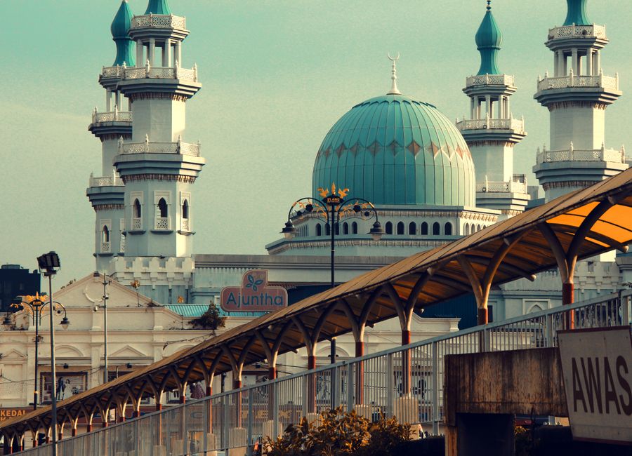A stunning view of a mosque with aqua domes and towering minarets, set against an urban backdrop.
