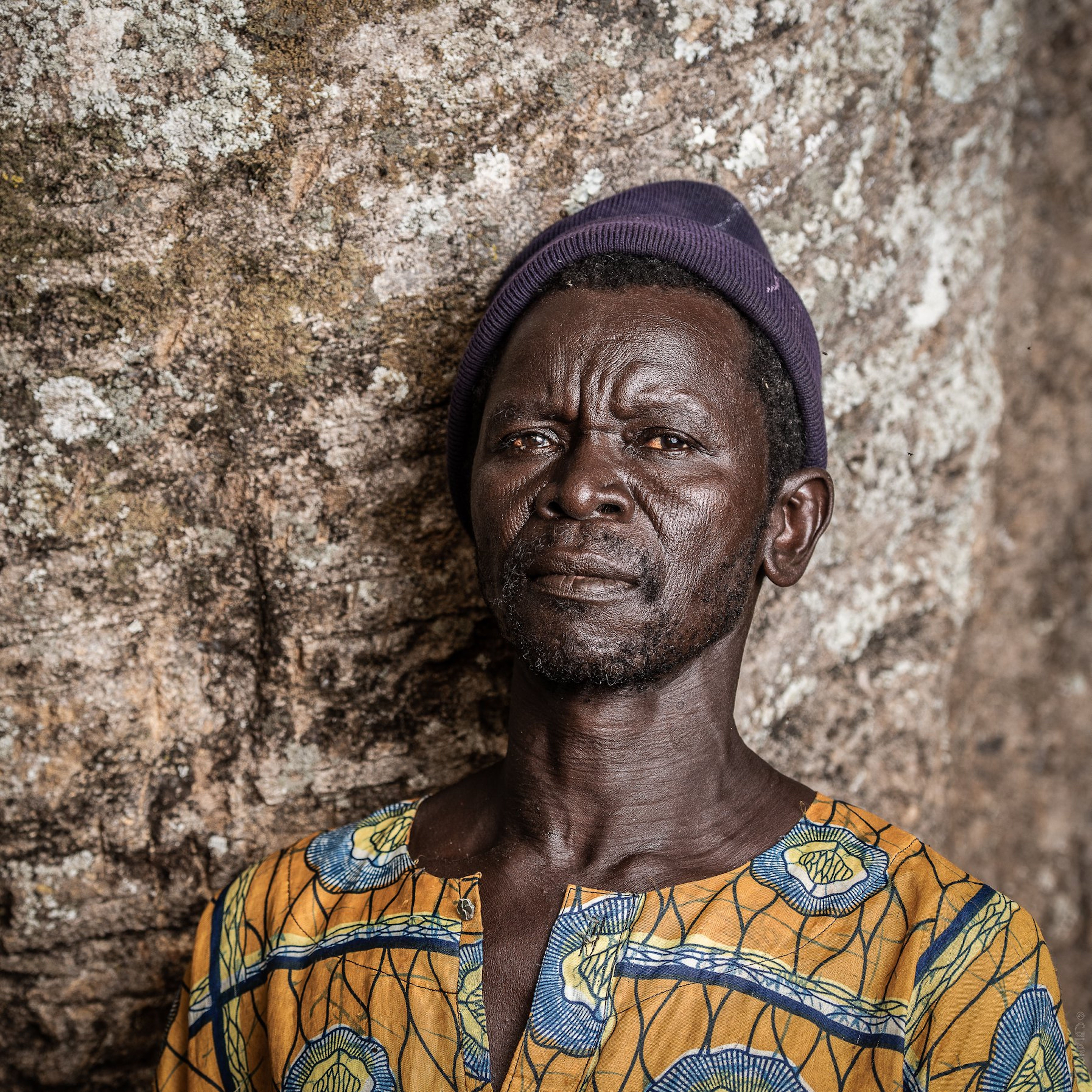 Portrait of an African man wearing traditional clothing in Benin City, Nigeria, against a stone wall.