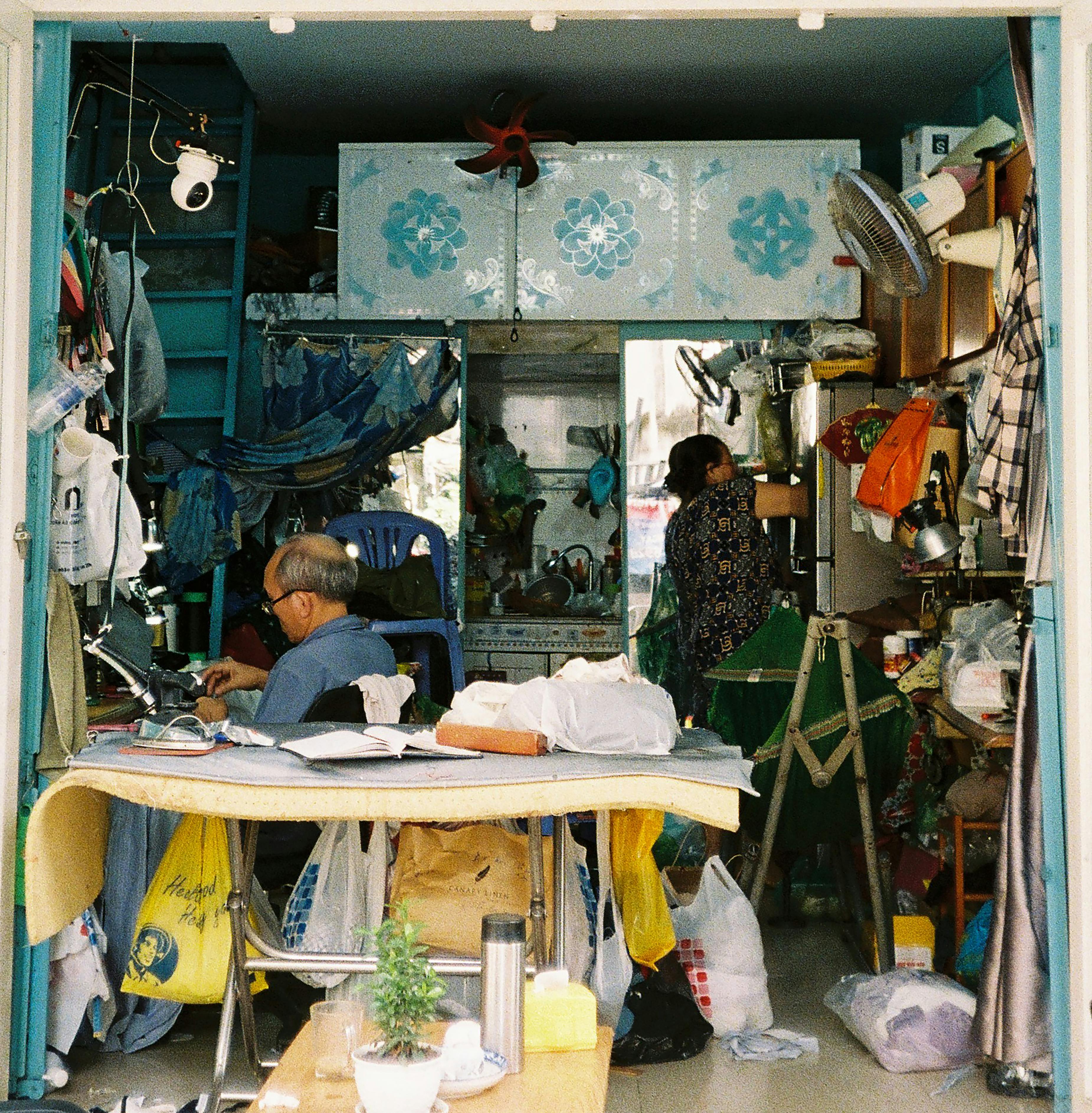 A bustling tailor workshop with two people engaged in sewing and organizing materials.