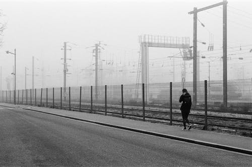 Candid Photo of a Woman Walking on the Pavement along the Railway 