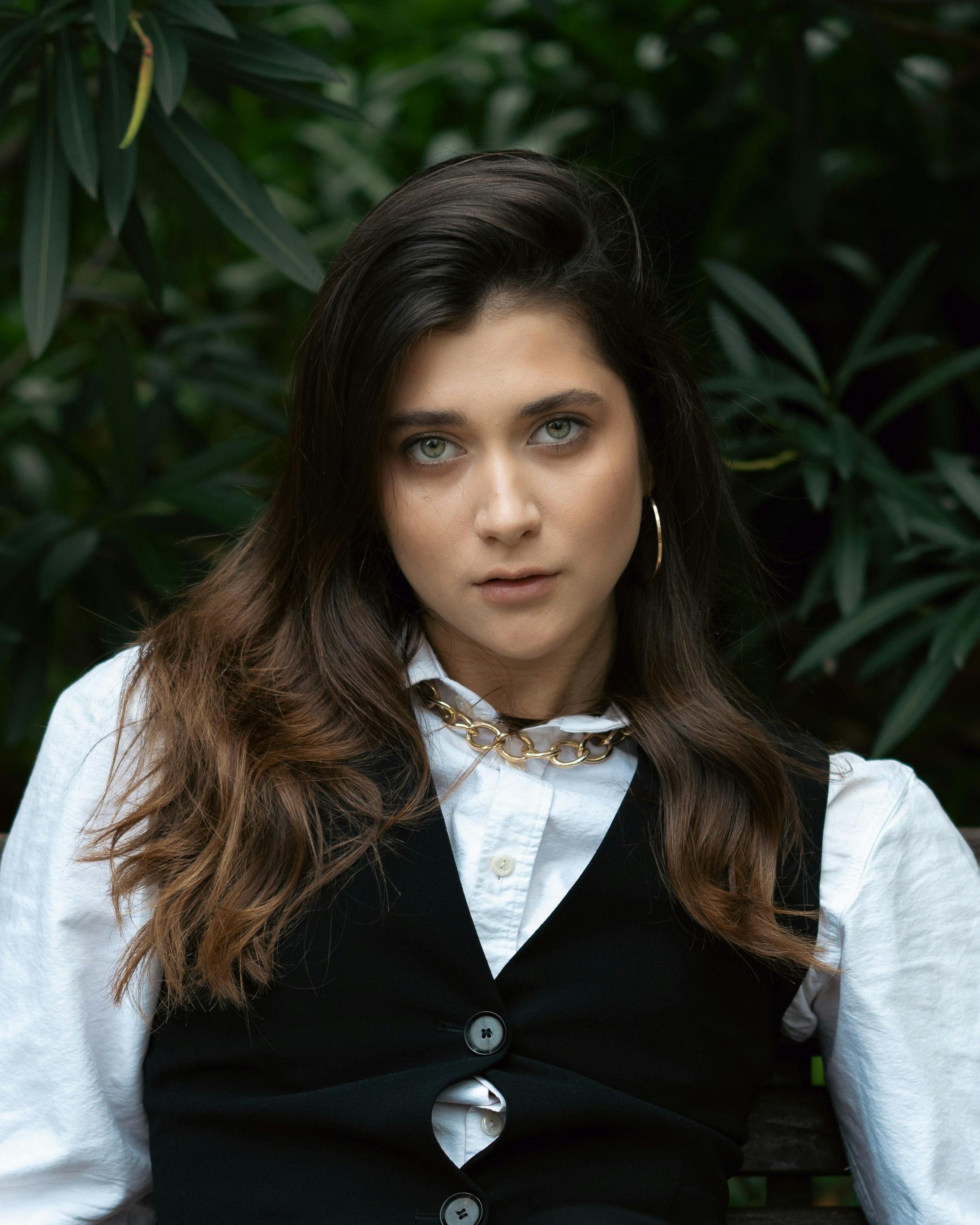 Portrait of a young woman in a black waistcoat and white blouse posing outdoors.