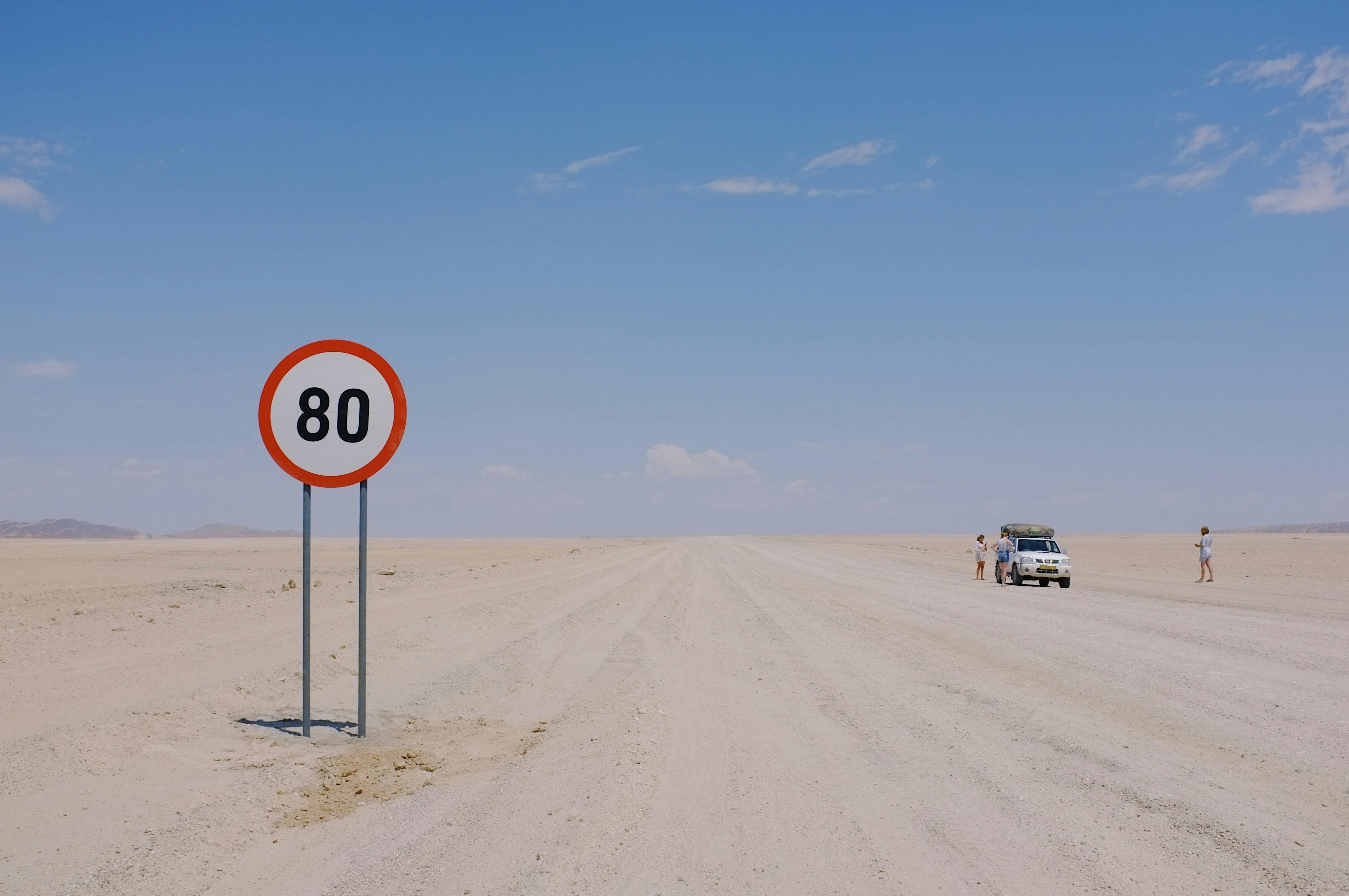 A distant desert road sign displaying 80km speed limit with a car and travelers visible.