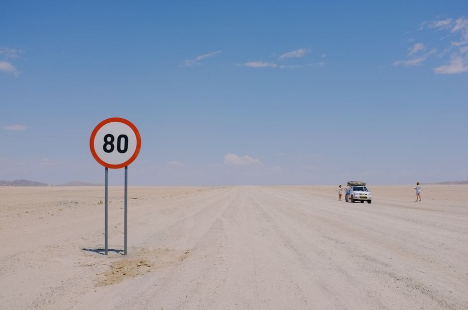 A distant desert road sign displaying 80km speed limit with a car and travelers visible.