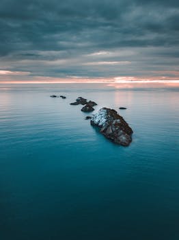 Aerial view of isolated rocky outcrops in a tranquil sea under a dramatic sunset sky.