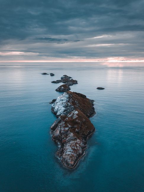 A breathtaking aerial view of a rock formation in the ocean under a dramatic evening sky.